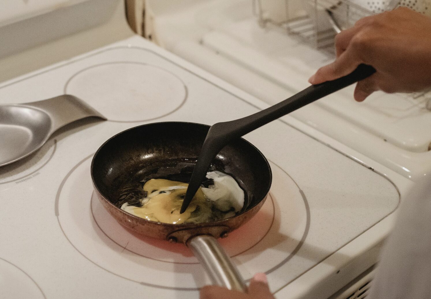 person cooking scrambled eggs with black utensils