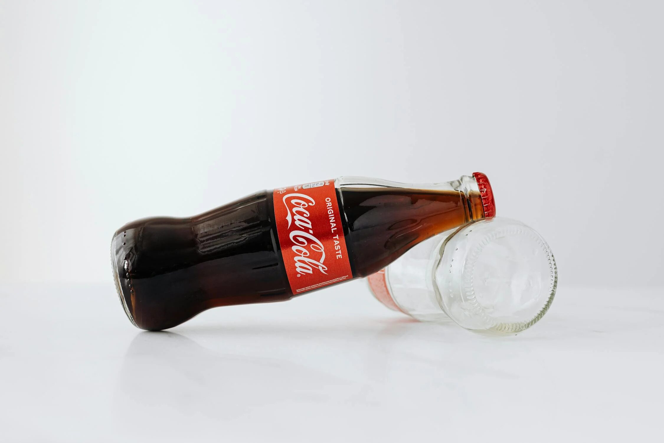 Glass bottle of cola with empty bottle on white surface