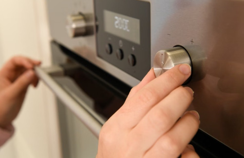 Close-up of hands adjusting the temperature dial on a modern kitchen oven.