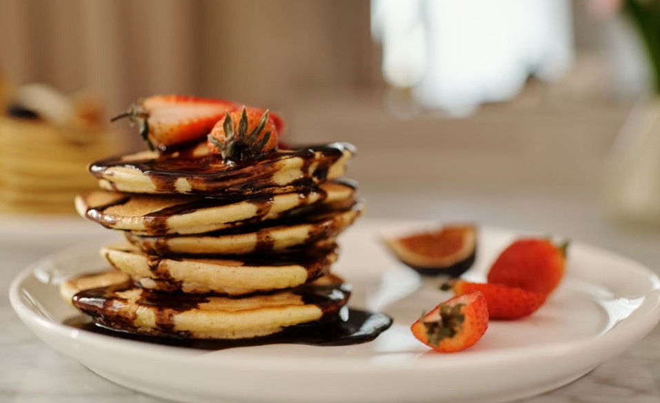 Close-up of a stack of pancakes drenched in chocolate syrup, topped with strawberries for a delicious breakfast.